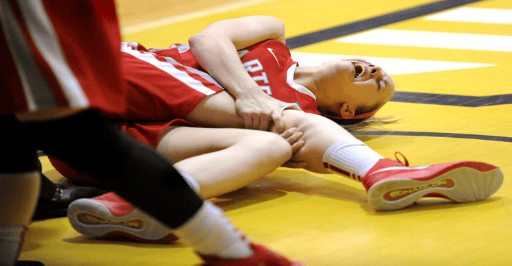 A basketball player lying on the court, holding her knee and crying out in pain