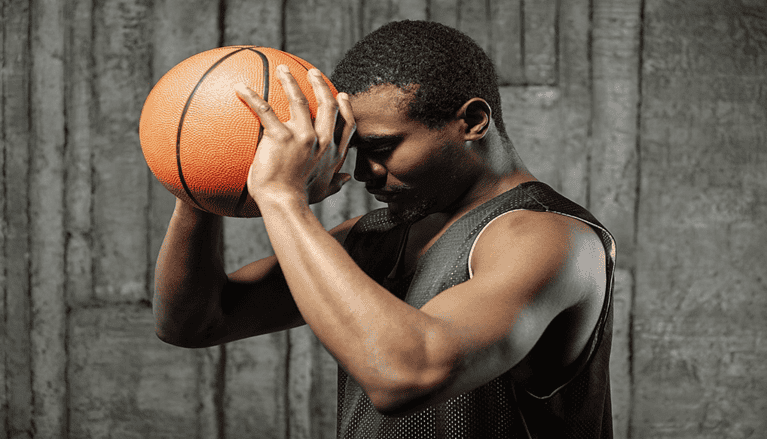 Basketball player resting a ball against his forehead with his eyes closed