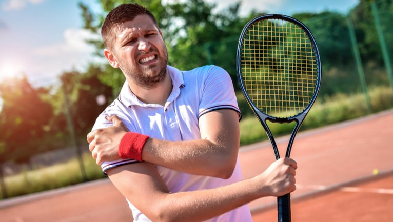 Tennis player holding his shoulder in pain while holding a racket