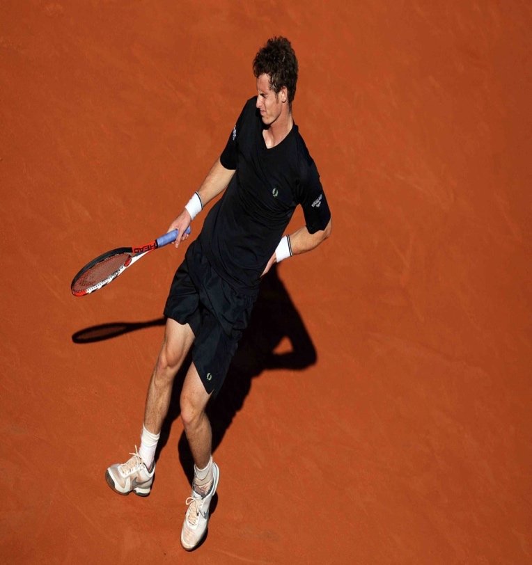 Tennis player serving on a clay court, seen from above