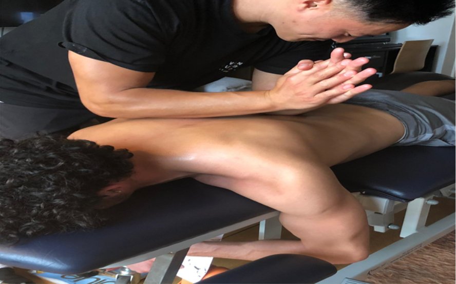 A practitioner leaning over a patient lying face down on a treatment table, hands clasped on the patient's upper back