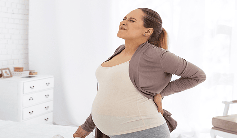 A pregnant woman wincing and holding her lower back