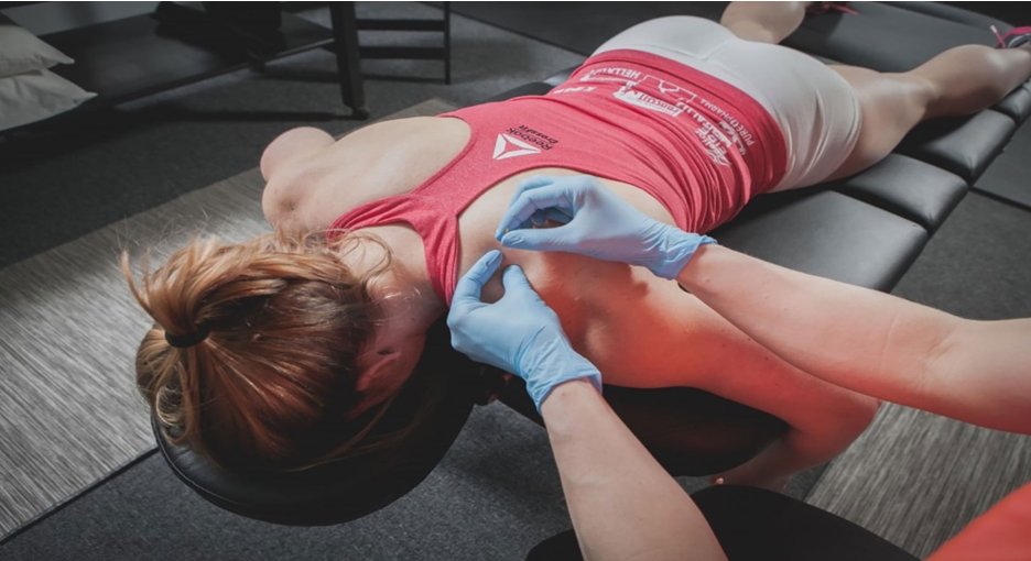 A gloved practitioner placing fine needles near the shoulder blade of a woman lying face down on a treatment table