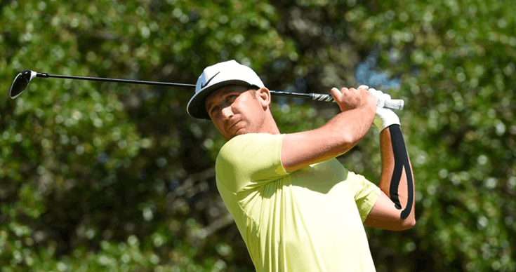 A golfer in a cap and yellow shirt following through on his swing, with tape on his forearm