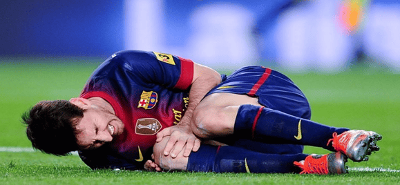 A footballer lying on the pitch, clutching his knee in pain