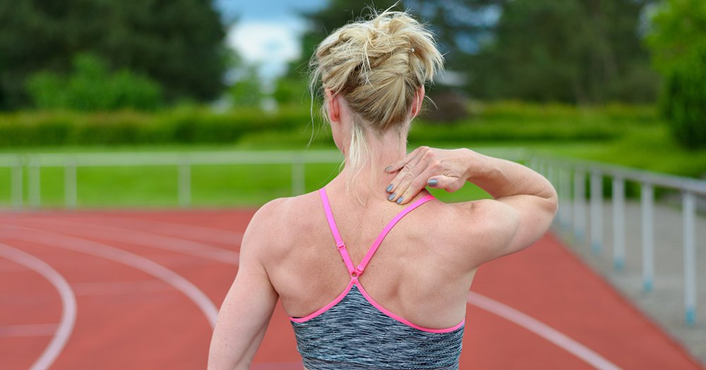 Woman on a running track reaching back to hold her shoulder