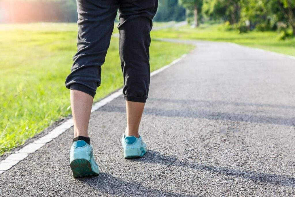 Close-up from behind of a person's lower legs and trainers walking along a park path