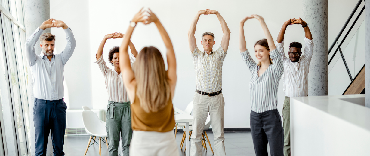 Office colleagues standing and stretching their arms overhead beside a meeting table.
