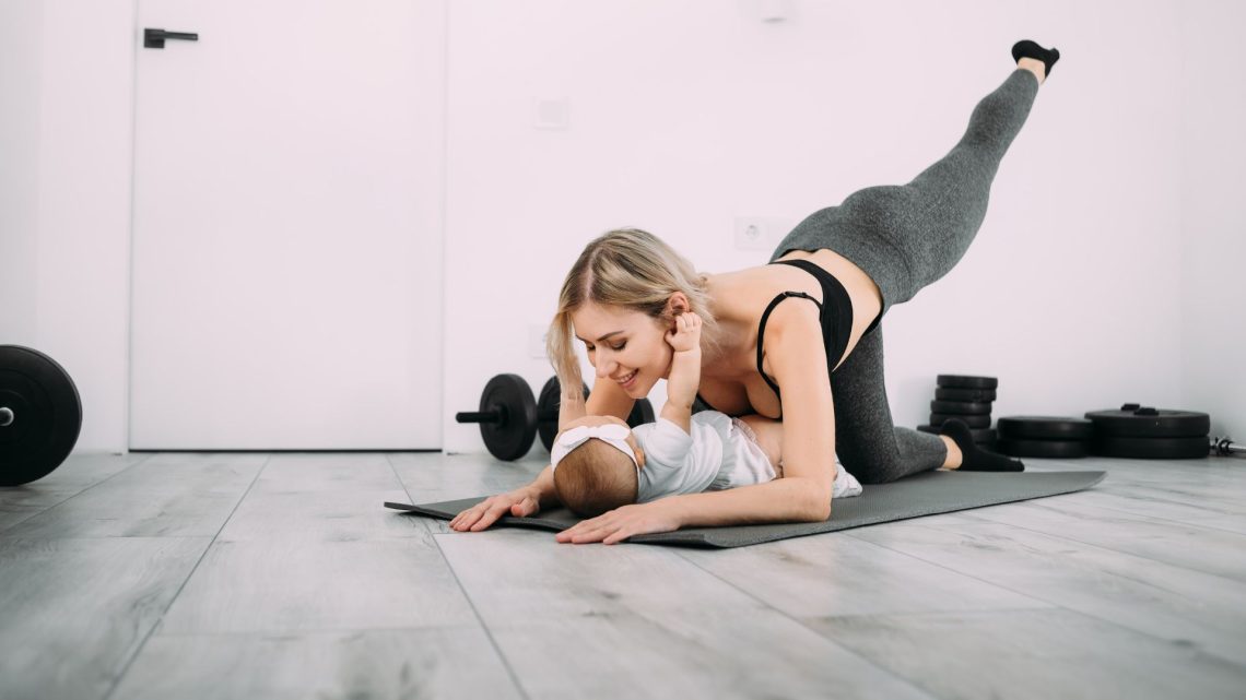 A woman exercising on a mat at home beside her baby.