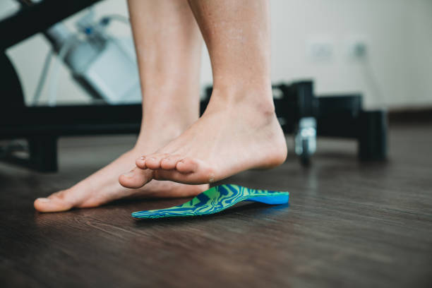 A bare foot standing beside a moulded orthotic insole on a wooden floor.