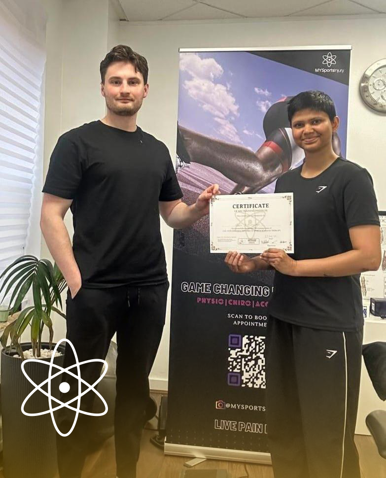 An MY Sports Injury clinician handing a printed course certificate to a graduate in the clinic, in front of an MSI roll-up banner reading Game Changing Physio, Chiro, Acu.